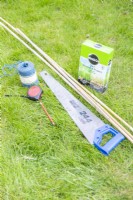 Granular fertiliser, bamboo canes, saw, twine, tape measure and a pencil laid out on the ground