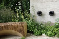 In a shady corner, view of the carved oak bench which is burnt and wire brushed, it seats by a water feature with ceramic water chutes, The Mind Garden - Designer: Andy Sturgeon - Sponsor: Project Giving Back.