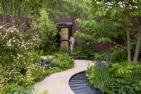 Water rill winding around planting of Iris sibirica, Primula, ferns and hostas, flowering Cornus kousa 'Cappuccino' - The Boodles Travel Garden, RHS Chelsea Flower Show 2022 - Gold Medal