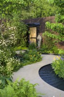 Curved path leading to doorway and water rill around  bed planted with Cornus kousa var. chinensis above shade-loving hostas, primulas, irises and disporum - The Boodles Travel Garden