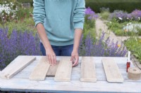 Woman using a small piece of wood as a spacer to evenly position the cut planks of wood