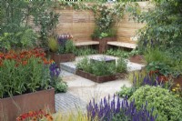 Simple wooden benches overlook a reflective water feature in Lunch Break Garden at RHS Hampton Court Palace Garden Festival 2022