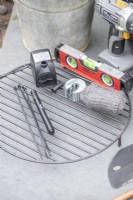 Boat level, water pump, pen, zip ties, pipe cutter, wire wool and metal grill laid out on the ground