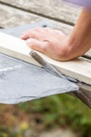 Woman using a length of wood and a file to break the slate along the scored line