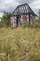 Burnt out Ukrainian Cottage in a field of barley in the What Does Not Burn garden at RHS Hampton Court Palace Garden Festival 2022