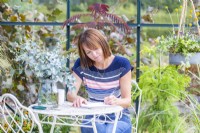 Woman sitting at table writing in a greenhouse filled with plants