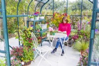 Woman sitting at a table reading in a greenhouse that has been filled with various plants and mixed containers