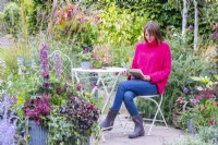 Woman sitting at a table reading on a patio surrounded by plants