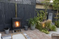 Log burner in patio area in suburban garden against black painted fence