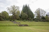 View across early-Victorian, grass terraces to Victorian Arboretum created amongst ancient woodland. Stone steps. 

Veteran Quercus robur syn. pedunculate oak, English oak and Castanea sativa syn. sweet chestnut flank an early Thuja plicata planted in 1863. 