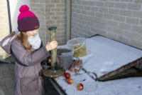 Girl holding bird feeder filled with sunflower seeds on snowy day in winter