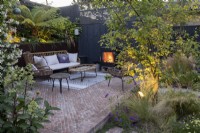 Patio area in suburban garden at sunset with lighting, seating and log burner