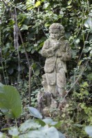 A weathered statue of a boy amongst overgrown and long grasses.  Autumn.