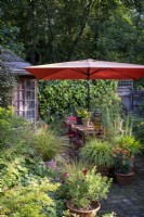 Small cottage style town garden built with wildlife in mind, large orange sunshade provides shade, and pots cover the paved patio