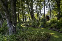 Shady woodland borders beneath trees in a summer garden, Gypsy caravan behind