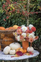 Autumn table decoration with selection of squashes arranged with bouquet of orange and white Dahlias and Chrysanthemums in orange pottery vase
