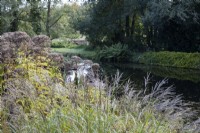 View over a variety of foliage and shrubs to a large pond. Regency House, Devon NGS garden. Autumn