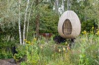 Bent oak swinging hide, suspended over naturalistic style planting, including Kniphofia, Rudbeckia 'Herbstonne' and Calamagrostis brachytrica - The Yeo Valley Organic Garden, RHS Chelsea Flower Show 2021