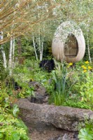 Bent oak swinging hide, suspended over naturalistic style planting with stream and stone bridge - The Yeo Valley Organic Garden, RHS Chelsea Flower Show 2021