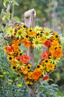 Summer wreath made of rudbeckia, nasturtium, sunflowers, pot and signet marigold hanging from the garden tool handle.