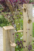 Wooden  bird -feeder with seeds on  spoons among perennials in  The Wooden Spoon Garden, RHS Hampton Court Palace Garden Festival 2022. Designers: Toni Bowater and Lucy Welsh