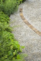 Winding gravel path with wooden pattern through perennial mixed planting in A Journey, in Collaboration with Sue Ryder garden at RHS Hampton Court Palace Garden Festival 2022