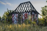 Burnt out Ukrainian Cottage in a field of barley in the What Does Not Burn garden at RHS Hampton Court Palace Garden Festival 2022 