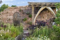 Mixed planting border with Echinacea purpurea alba in front of bespoke pergola in The Blue Diamond Group Beautiful Abandonment garden at RHS Hampton Court Palace Garden Festival 2022