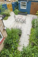 Aerial view of a modern patio garden in summer with plants chosen to encourage insects. Erysimum, geraniums, lavender, echinops, veronicastrum. Mosaic folding table and chairs, bee barrel hanging on wall. June.