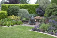 Seating area with water feature bordered by mixed beds of shrubs and summer flowers - June