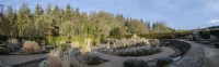 Winter garden with foliage and grasses, strong design of walls built in stone and water rills between.