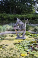 Dragon sculpture in pond with algae and water lilies.August. Summer