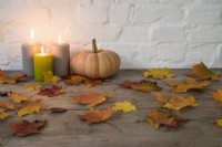 Trio of lighted pillar candles and 'Autumn Crown' pumpkin with autumn leaves on wooden background