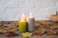 Trio of lighted pillar candles with autumn leaves and 'Autumn Crown' pumpkin on wooden background