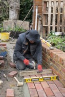 A worker laying bricks for a curved stone path around a raised bed during the makeover of a small London Garden.