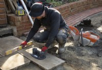 A worker laying slabs of York Stone for a terrace during the makeover of a small London garden.