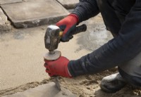 A worker cutting a thick piece of York Stone being used to construct a terrace in the makeover of a small London garden.