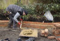 A bricklayer building a low curved brick wall around a raised bed during the makeover of a small London Garden.
