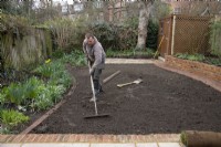 A worker raking the ground in preparation for laying new turf during the makeover of a London garden.