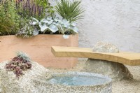 Drought tolerant garden with stone water feature, sculptural wooden bench set on stone and rendered wall. Curved terracotta planters with Arbutus, Salvia and Senecio candidans 'Angels Wings' - A Mediterranean Reflection, RHS Chelsea Flower Show 2022 - Silver Medal