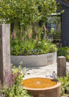 Contemporary water feature set in modern garden with upright wooden posts and conrete container with tree underplanted with perennials, summer June
