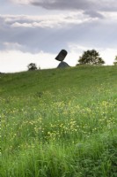 Stonebalancing sculpture by Adrian Gray in a Wiltshire garden in May with meadow of buttercups in the foreground.