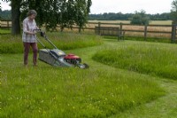 Woman mowing paddock leaving areas for wildlife and wildflowers to flourish