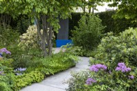 A stone path winds deeper into a therapeutic green space, passing between borders of herbaceous perennials, into the shade of Parrotia persica and to colourful, sheltered seating areas.