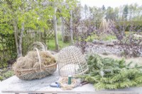 Dried grass, moss, pine branches, bamboo cloche, chicken wire, wire, secateurs, wire cutters and rope laid out on table