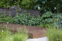 Centre for Mental Health's The Balance Garden. Designers: Jon Davies and Steve Williams. Chelsea Flower Show 2023. Climate resilient garden with edible plants and weeds for wildlife diversity. Raised rusty steel walkway. Summer.