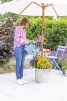 Woman watering weighted plant container with parasol inside