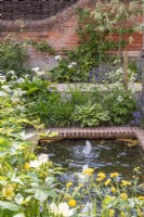 Small rectangular brick lined pool with bubble fountains with borders, plants inc:- Hostas; Astrantia; Zantedenchia aethiopica; Tulbaghia violacea, Geums