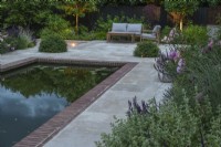 Garden lighting on sandstone terrace with rectangular pool and furniture, Pittosporum topiary balls for light concealment