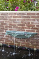 Verdigris metal basin fountain on brick wall 